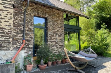 Das Bild zeigt einen Ausschnitt der Vorderseite der renovierten Mühle. Dort steht eine Hängematte vor einer Fensterfront.